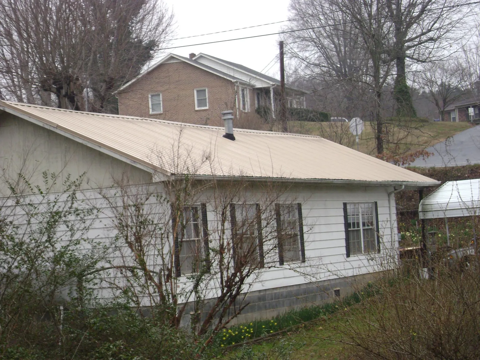 Tan metal roof on a white sided house set into a hillside — Commercial Roofing by Roofing Brothers in Santa Monica